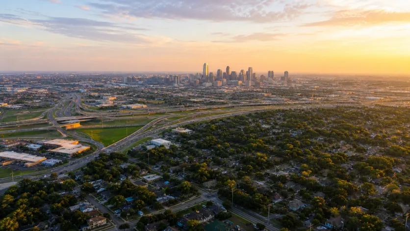 Aerial view across North Texas suburbs toward a city skyline at dawn. Conceptual imagery — not an active listing.